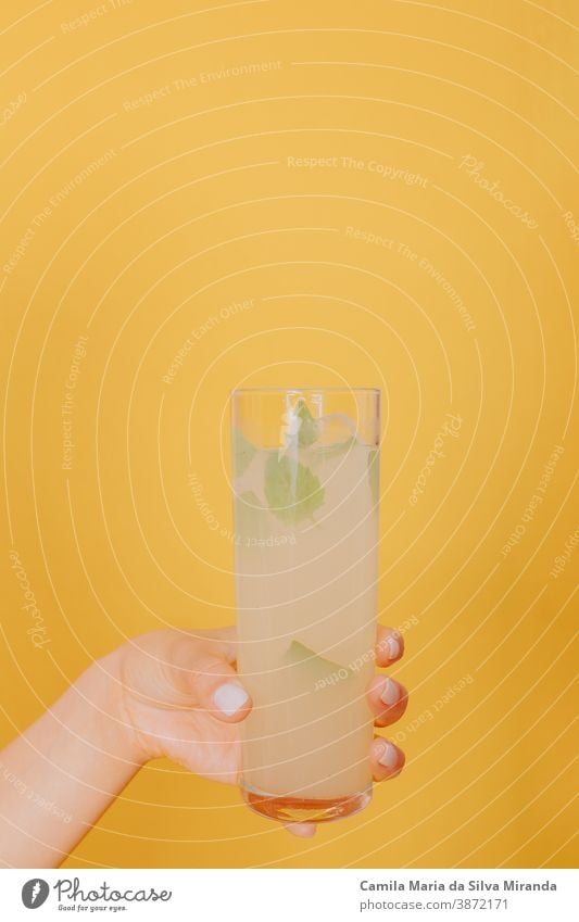 Young woman hand holding a glass of cocktail with mint. Studio photo with yellow background. alcohol beverage celebration citrus closeup copy space drink fresh
