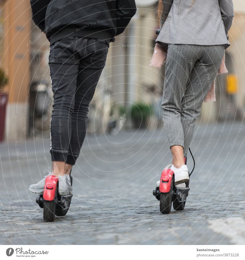 Rear view of unrecognizable trendy fashinable teenagers riding public rental electric scooters in urban city environment. New eco-friendly modern public city transport in Ljubljana, Slovenia.