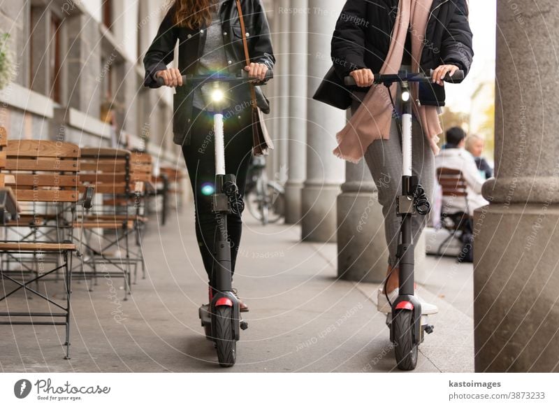 Unrecognizable trendy fashinable teenager girls riding public rental electric scooters in urban city environment. New eco-friendly modern public city transport in Ljubljana, Slovenia