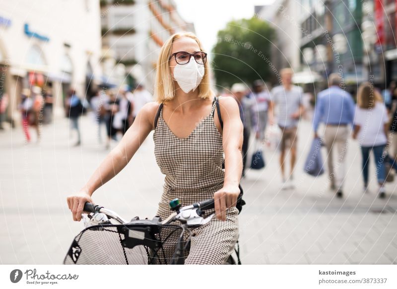 Woman riding bicycle on city street wearing medical face mask in public to prevent spreading of corona virus. New normal during covid epidemic. covid-19 woman