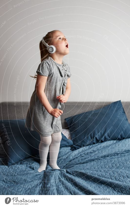 Little girl singing dancing imitating herself a real singer child jumping playing listening fun happy home bed childhood portrait natural dance pretend