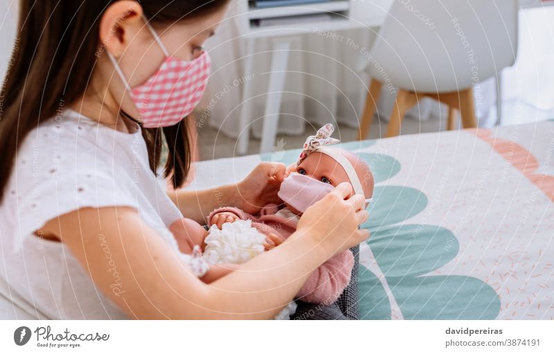 Girl with mask putting small mask on her doll girl playing putting mask face covid-19 coronavirus generation care people lockdown child female health protective