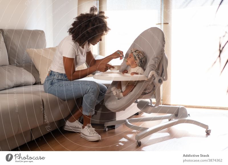 Mother feeding little baby at home eat toddler mother child food help childcare ethnic black african american lunch domestic parent relax cute comfort bonding