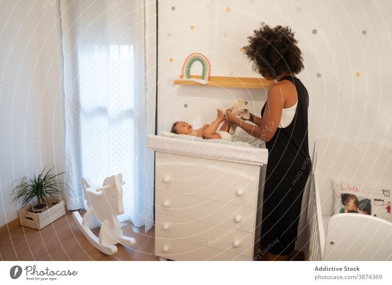 Black woman putting on clothes on baby change table mother put on pants care toddler little ethnic black african american lying home parent child tender