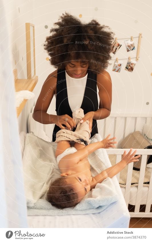 Black woman putting on clothes on baby change table mother put on pants care toddler little ethnic black african american lying home parent child tender