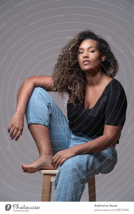 Stylish black woman in casual wear sitting on chair fashion plus size overweight jeans style barefoot model curly hair young african american ethnic female