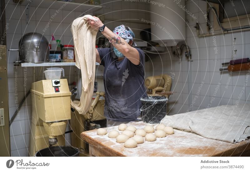 Woman kneading dough in bakehouse bread bakery raw work prepare kitchen female mask new normal cook food chef fresh culinary cuisine pastry ingredient recipe