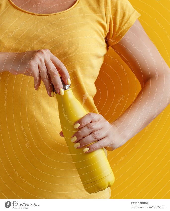 Close up of woman holding yellow reusable bottle on yellow background hand monochrome ecologic water steel thermo open bright mockup faceless aluminum blank
