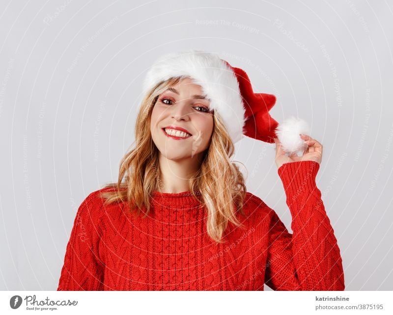 Smiling Young woman in Santa hat touching hat pom pom santa hat hands christmas smile white isolated red grey close up sweater Holiday celebration season Xmas