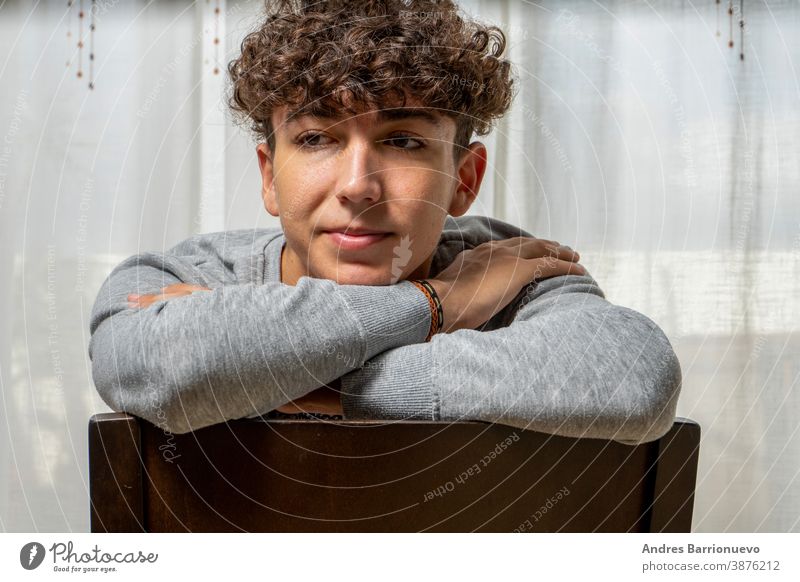 Attractive young man with curly hair wearing gray sweatshirt posing on white  curtains background - a Royalty Free Stock Photo from Photocase