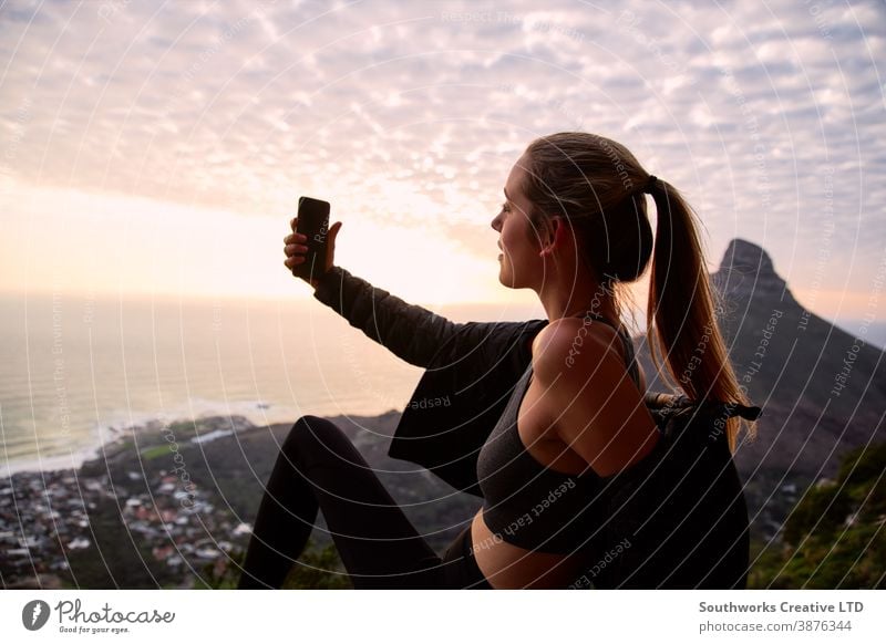 Young Woman With Backpack Hiking Along Coastal Path Posing For Social Media Selfie On Mobile Phone selfie sunset woman young women hike hiking walk walking