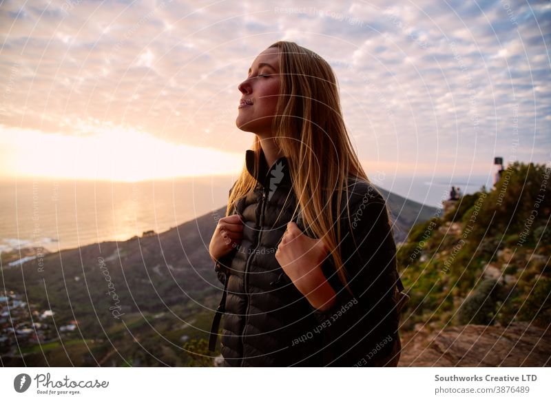 Portrait Of Woman Closing Her Eyes As She Hikes Along Coastal Path And Sun Sets Over Sea Behind Her sunset woman golden hour freedom young women hike hiking