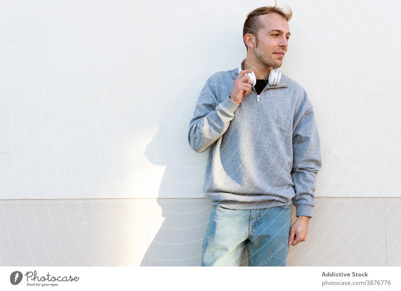 Young man with headphones looking away sunlight sunshine cover protect hipster urban male modern unshaven casual wall street lifestyle street style guy young