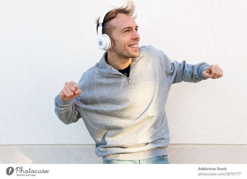 Optimistic man with headphones dancing on street dance optimist cheerful music hipster happy energy urban young male casual wall listen lifestyle sound song joy