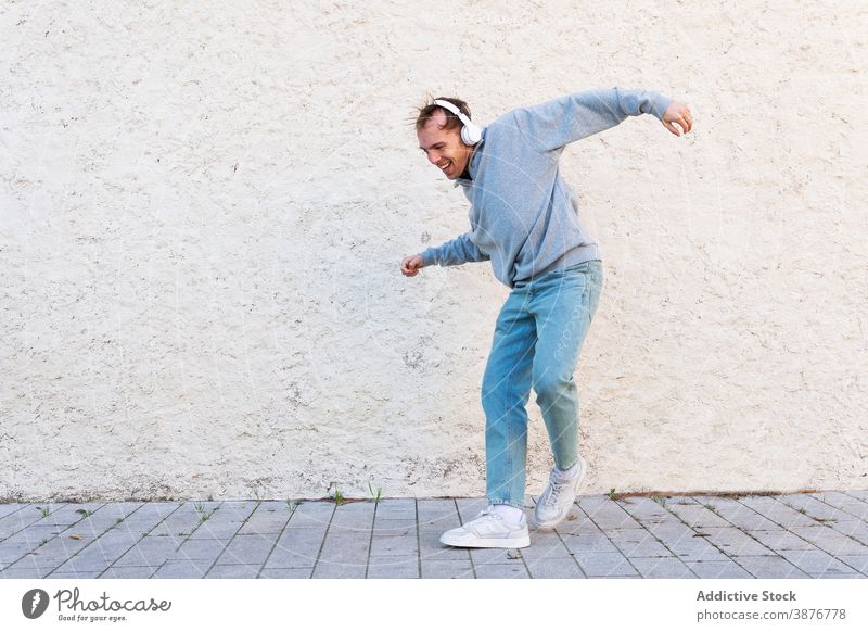 Optimistic man with headphones dancing on street dance optimist cheerful music hipster happy energy urban young male casual wall listen lifestyle sound song joy