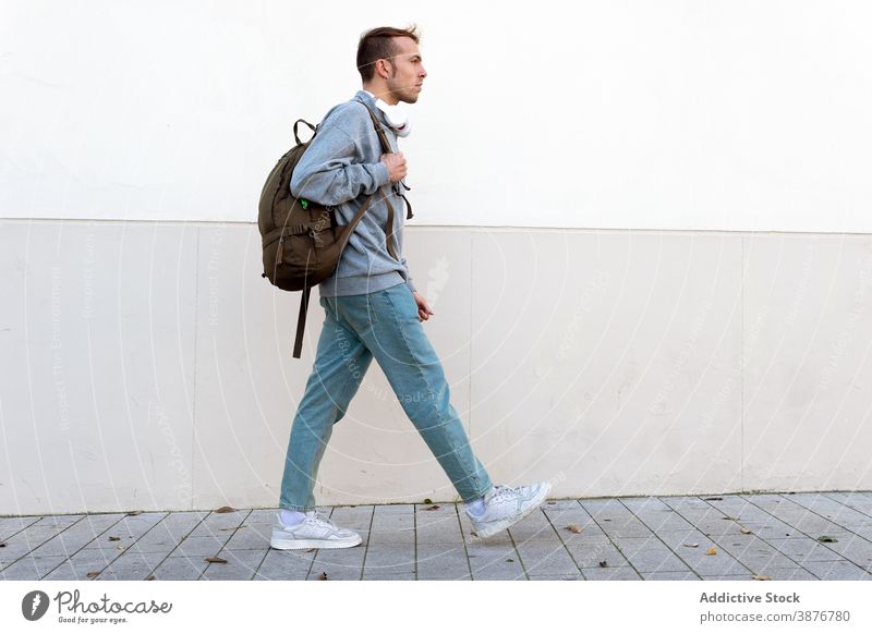 Young man with backpack walking near wall hipster casual urban modern style trendy young male lifestyle guy pedestrian traveler millennial active commute