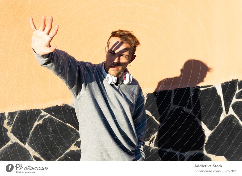 Young man with headphones covering face from sunlight sunshine protect outstretch hipster urban male modern unshaven casual wall street lifestyle street style