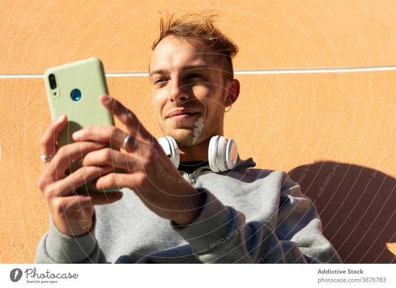 Young hipster man browsing smartphone using wall urban positive online young guy casual headphones mobile sunny shadow gadget connection male lifestyle street