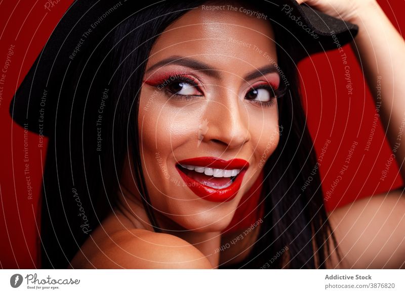 Smiling woman with red lips in studio makeup visage charming appearance hat touch head model cheerful female smile optimist positive content vivid vibrant