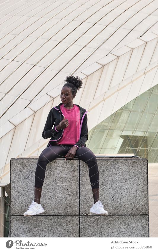 Serious black sportswoman sitting on stone border in city athlete determine confident runner street serious fit sportswear female ethnic african american