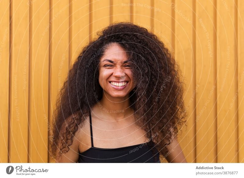 Cheerful black woman with curly hair in street afro hairstyle smile portrait sincere candid young female ethnic african american delight joy wooden wall relax