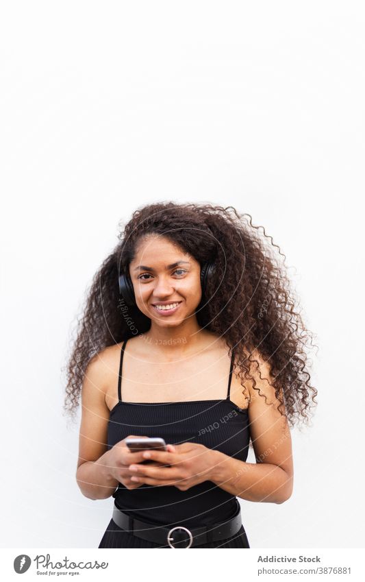 Optimistic black woman listening to music on street headphones meloman enjoy afro hairstyle curly hair smartphone female ethnic african american city sound