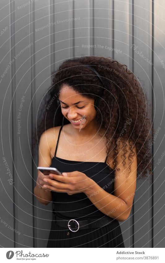 Optimistic black woman listening to music on street headphones meloman enjoy afro hairstyle curly hair smartphone female ethnic african american city sound