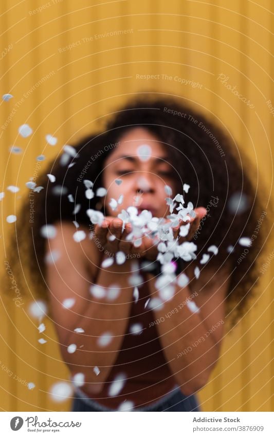 Black woman blowing confetti towards camera festive celebrate concept having fun event curly hair afro female ethnic black african american hairstyle holiday