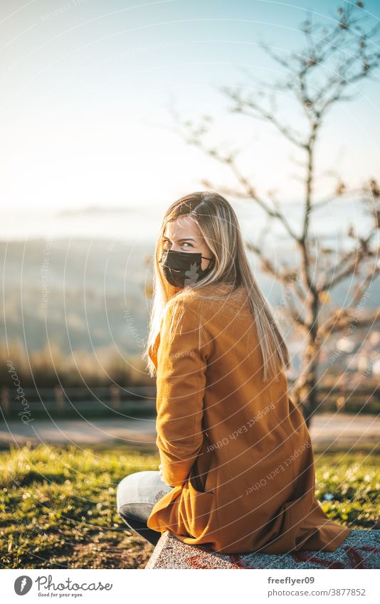 Woman on a yellow coat sitting on a bench with a face mask woman coronavirus covid winter autumn contemplating vigo galicia nature outdoors freedom sunset