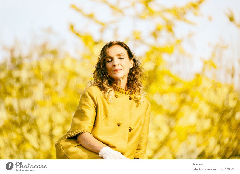 woman resting in the park during autumn retouching hair leaves yellow garden yellowish leafs lifestyle mature portrait one people tree coat yellow overcoat
