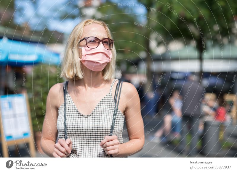 Portrait of casual yound woman walking on the street wearing protective mask as protection against covid-19 virus. Incidental people on the background city face
