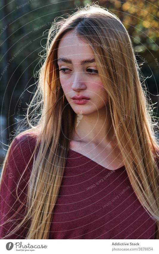 Long haired young woman looking at camera in park long hair blond confident modern autumn portrait natural teen female style teenage millennial fair hair lady