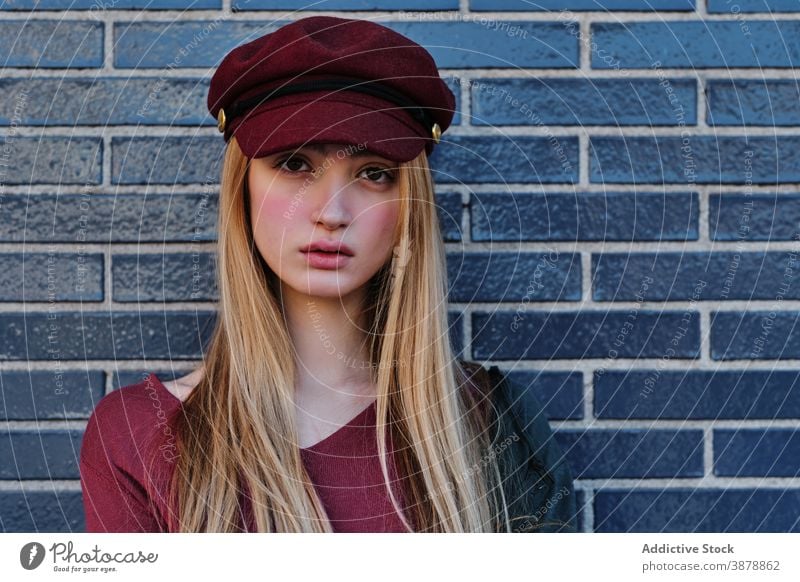 Trendy young woman in autumn outfit standing near wall style fashion cap color red trendy modern female urban casual hipster headgear headwear blond cloth vogue