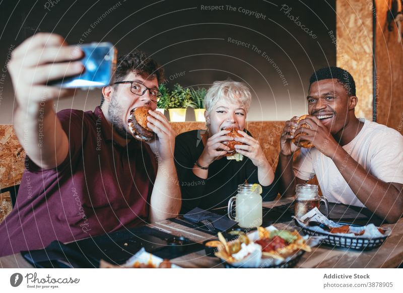 Company of friends taking selfie with burgers in cafe eat people having fun fast food junk food cheerful multiethnic diverse multiracial black african american