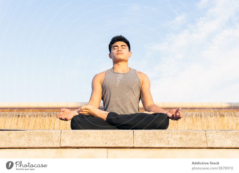 Focused man practicing meditation on lotus pose yoga city stress relief asian mindfulness mental tranquil ethnic male concentrate practice energy wellness