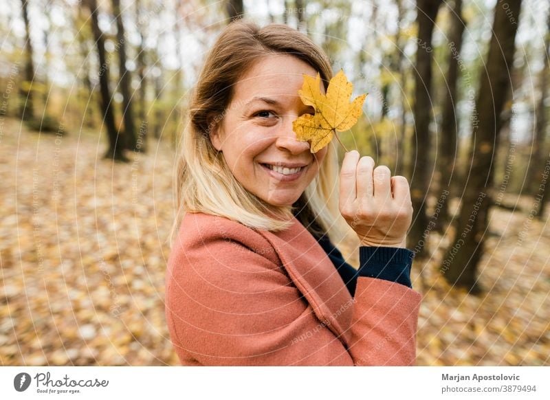 Young woman holding yellow autumn leaves in the forest 30s adult beautiful beauty blonde caucasian cheerful color cute enjoy fall female foliage fresh fun girl