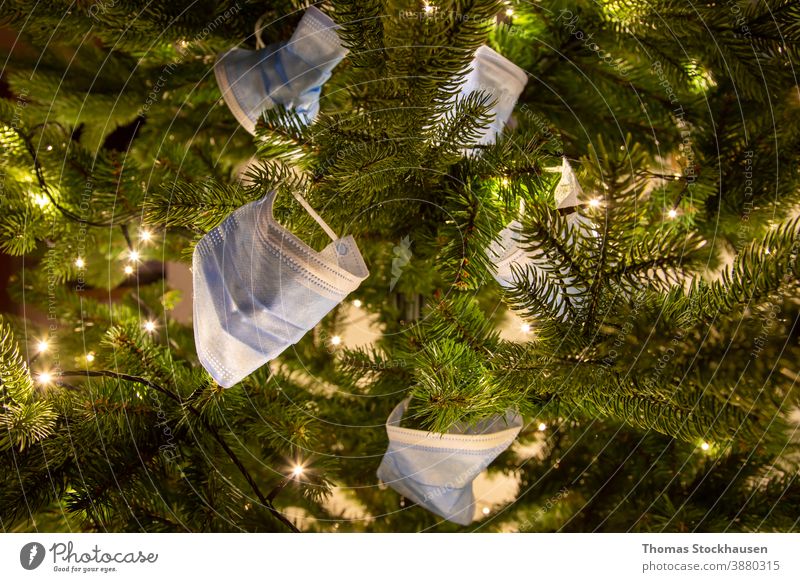 several mouth protection mask on a pine tree branch, lights in the background. Symbol for impact of covid-19 virus in christmas season 2020 and 2021 abstract