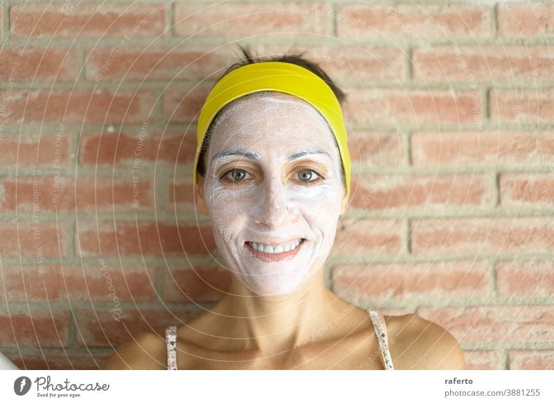 Relaxed woman applies mineral clay mask on face for rejuvenation, has headband on head skincare cosmetic female healthcare beauty person healthy clean beautiful