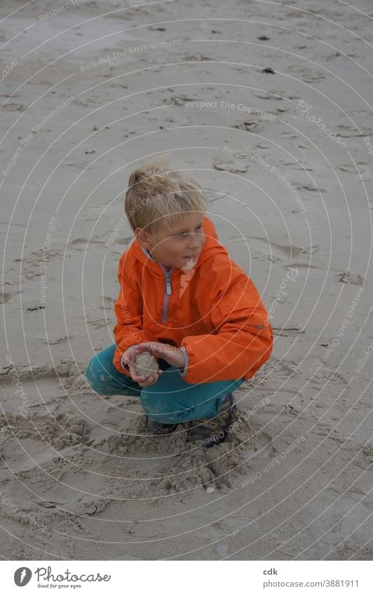 Childhood | sandy affair. Boy (child) Blonde squatting in the sand by the sea orange windbreaker Orange Turquoise holidays sandballing monitoring