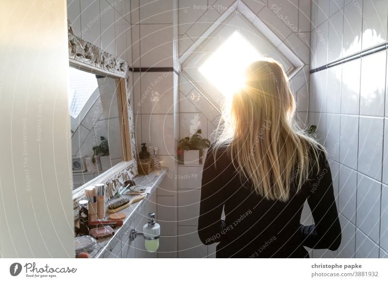 Rear view of a blonde woman standing in a bathroom Woman Blonde Back-light Bathroom Sunlight care hygiene indoors Tile Colour photo Interior shot Mirror White
