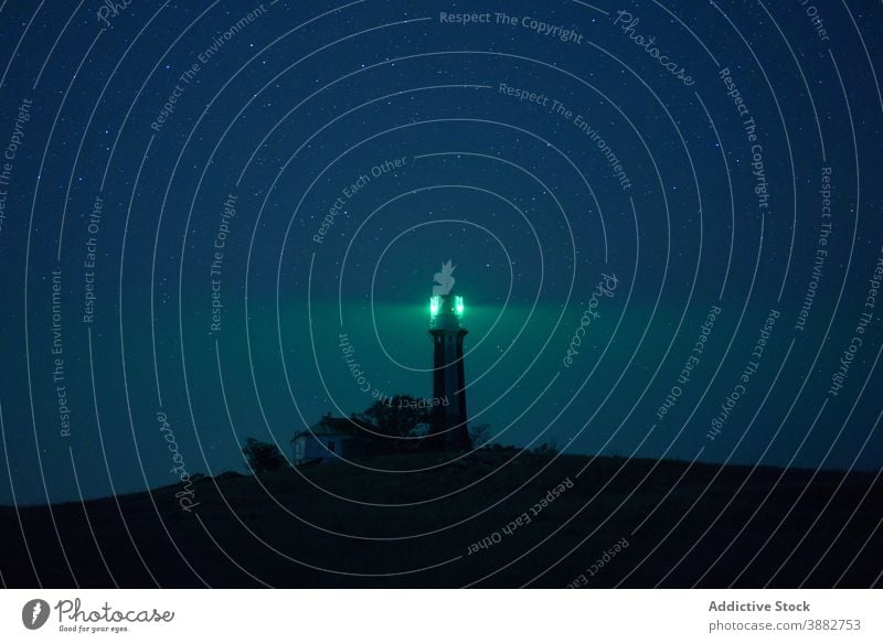 Lighthouse glowing at night against starry sky lighthouse beacon hill tower illuminate green landscape nature picturesque twilight architecture spectacular