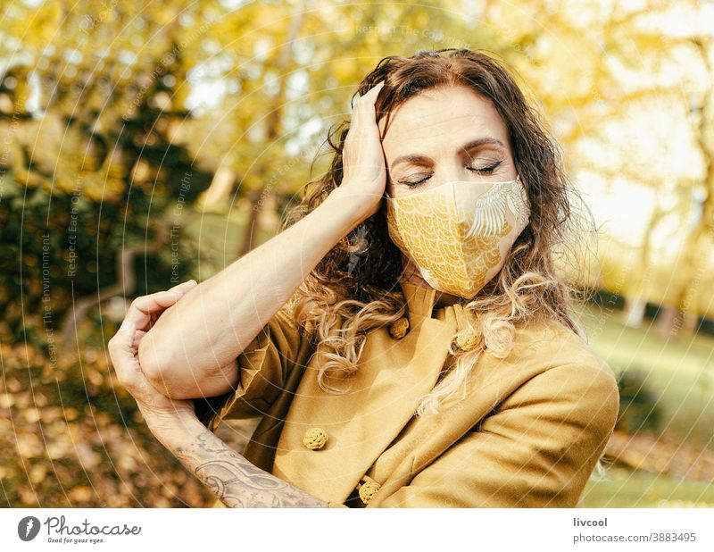 woman in yellow dress and mask in a park II retouching hair garden yellowish leafs lifestyle mature portrait one people tree coat yellow overcoat scene romantic