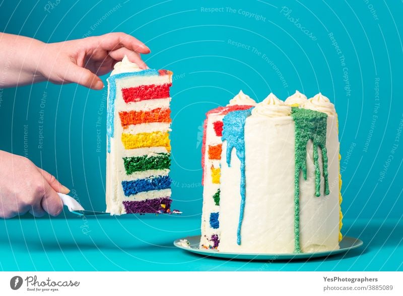 Woman taking a slice of cake. Homemade rainbow cake on blue background bakery birthday birthday cake buttercream celebration close-up colorful confectionery