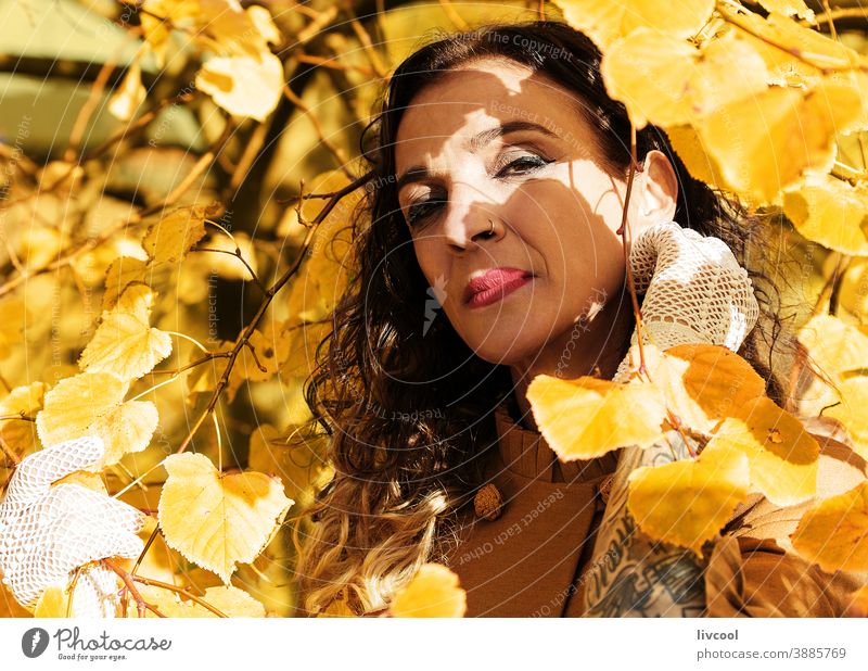 woman among the branches of a golden tree in autumn retouching hair yellow park garden yellowish leafs lifestyle mature portrait one people coat yellow overcoat