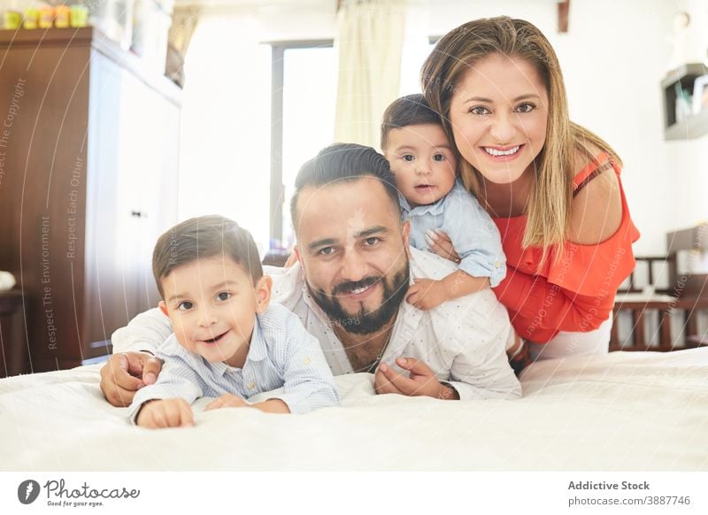 Cheerful ethnic family on bed at home gather having fun pastime together couple son sibling hispanic relationship love fondness kid child cuddle affection enjoy