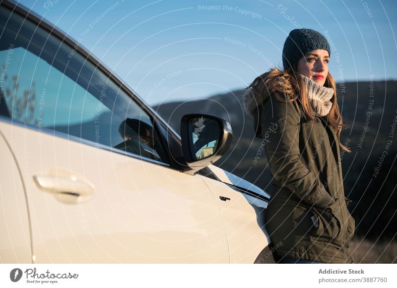 Woman standing on road near car and enjoying weather sun woman warm clothes tranquil carefree cold season female auto automobile roadway happy positive content