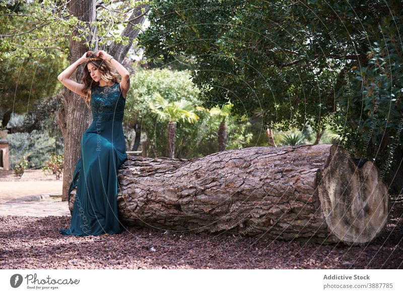 Tender woman in long emerald dress in forest grace elegant woods nature tranquil dreamy carefree tree trunk sit maxi young style woodland calm lady summer