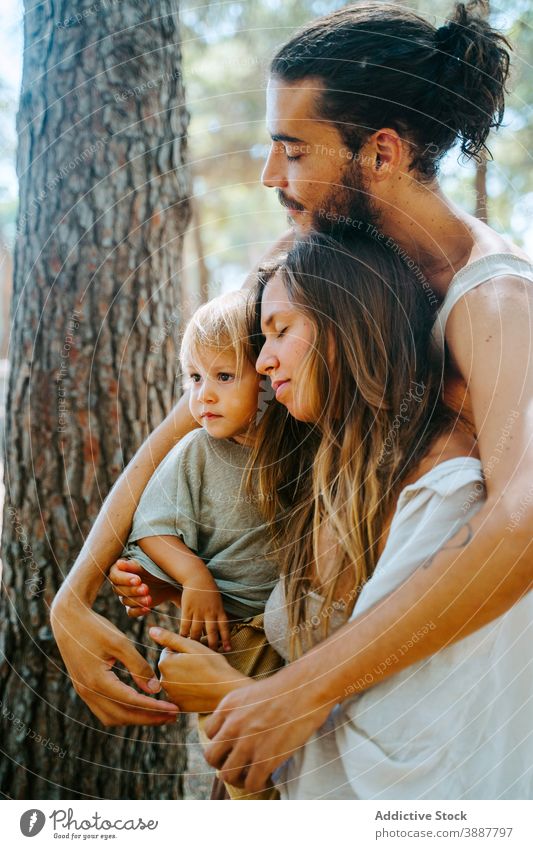 Happy multiethnic family hugging with eyes closed in forest woods weekend together toddler kid love unity multiracial diverse nature embrace relationship