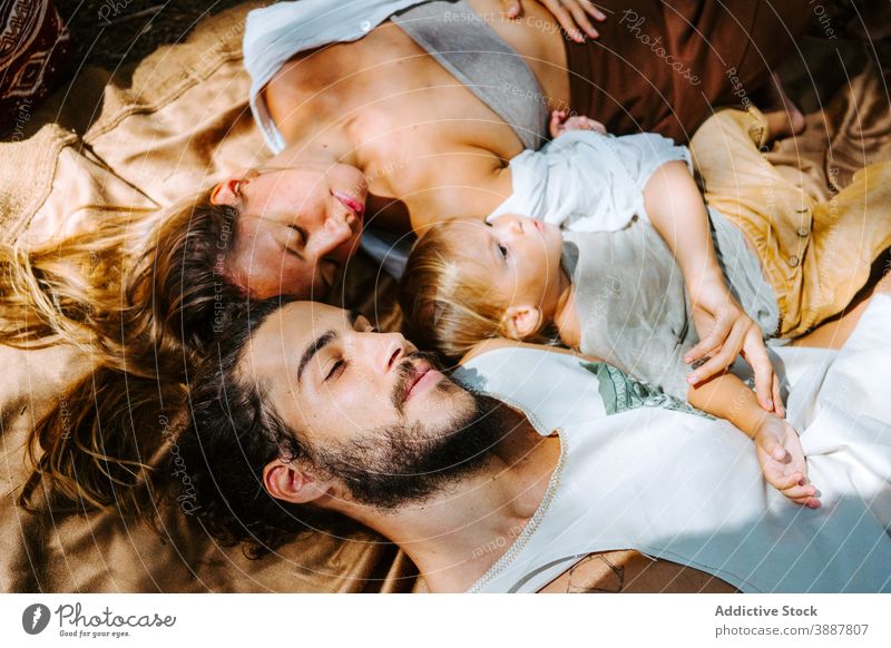 Gentle family relaxing together in nature blanket hippie care lying tender sunlight multiracial multiethnic diverse cute toddler sunny affection rest summer