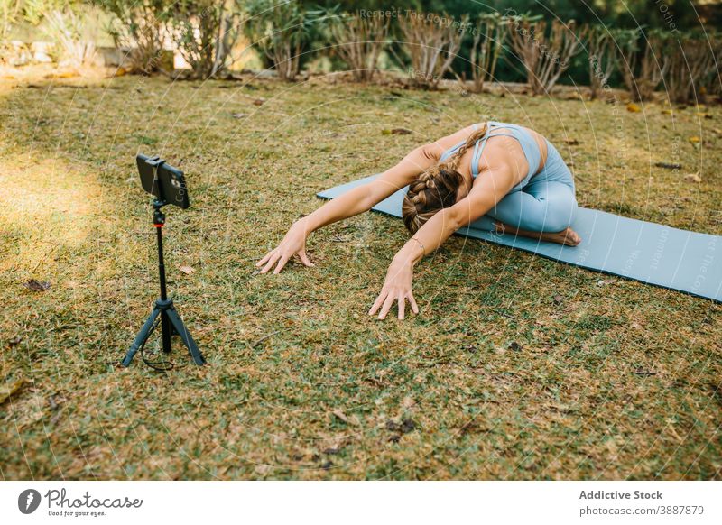 Flexible woman doing yoga in Bound Angle pose blogger video record smartphone influencer bound angle pose asana female mobile mat summer tutorial cellphone park